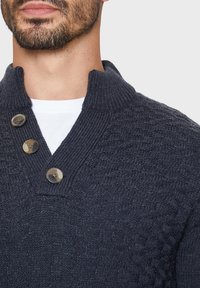 Navyblauwe gebreide trui met een textuurpatroon, een hoge kraag en een drieknoopsluiting bij de hals. Gladde stof met ribbelaccenten.