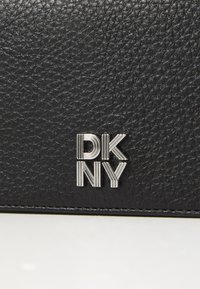 Must mustril nahkrahakott hõbedase DKNY logoga. Omab siledat viimistlust ja peent mustrit materjalil.