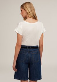 Cămașă albă cu mânecă scurtă și guler rotund, asortată cu șorturi din denim albastru închis, având curea și buzunare la spate.