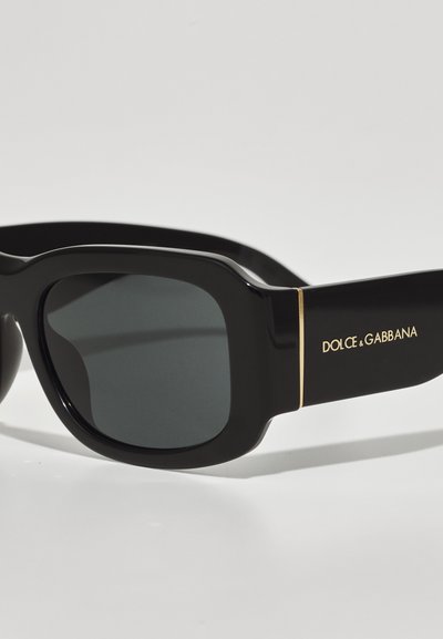 Ochelari de soare negri cu un finisaj lucios, lentile pătrate și accente aurii pe braț, având marca "DOLCE & GABBANA".