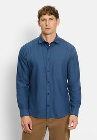 Blaues Hemd mit Knopfleiste aus strukturiertem Stoff, mit Brusttasche, langen Ärmeln und abgerundetem Saum. Kombiniert mit beigen Hosen.