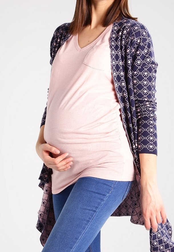 En marinblå tryckt kofta som bärs över en ljusrosa V-ringad skjorta, tillsammans med blå jeans, som framhäver en rund mag silhuett.