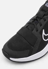 Scarpa sportiva nera con tomaia in mesh testurizzato, un logo bianco a contrasto e un sistema di allacciatura piatta con cinturino per una vestibilità sicura.
