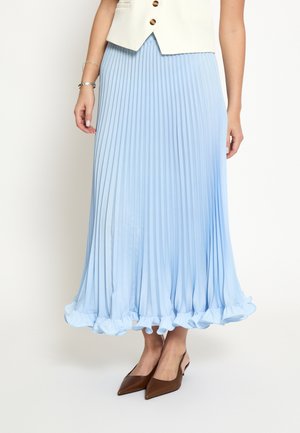 Donna che indossa una gonna midi plissettata azzurro chiaro con orlo arricciato, gilet bianco senza maniche e scarpe slingback marroni con punta affilata.