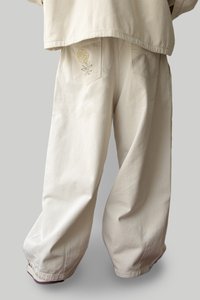 Pantalon large beige avec une texture douce, doté d'une broderie florale sur la poche arrière. Design décontracté avec une coupe relaxée.
