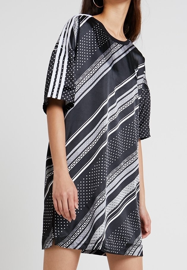 Svart oversized t-shirt klänning med vita mönster, diagonala ränder och prickar. Har korta ärmar och en mjuk tygtextur.