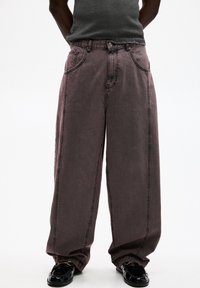 Jeans a gamba larga di un colore mauve scolorito, realizzati in denim con cuciture visibili, dotati di due tasche frontali e chiusura con bottone.