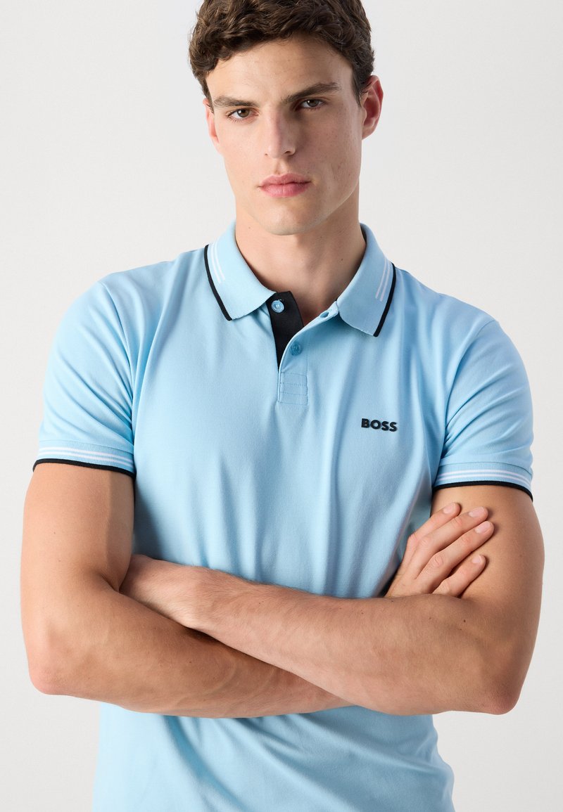 Polo bleu clair avec des finitions noires et blanches, manches courtes, et logo "BOSS" brodé sur la poitrine, fabriqué à partir d'un tissu lisse.