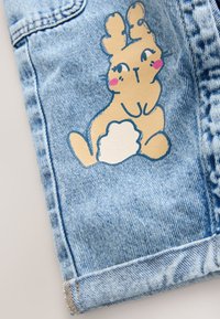 Lyseblåt denimstof med et tegneserieagtigt brun kanin-design med lyserøde kinder og hvid fluffy hale, trykt på benet.