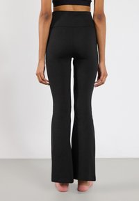 Zwarte flared leggings van rekbare stof, met een hoge tailleband en een soepele textuur, aansluitend op de dij en uitlopend aan de onderkant.