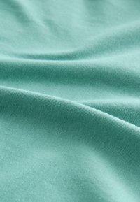 Glattes helltürkisfarbenes Gewebe mit weichen Falten und sichtbarer feiner Strickstruktur unter gleichmäßiger Beleuchtung.