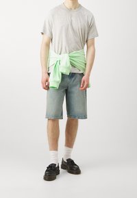 Šedé tričko, volné světle modré denimové kraťasy, mentolově zelená mikina uvázaná v pase a černé boty s tlustou podrážkou.