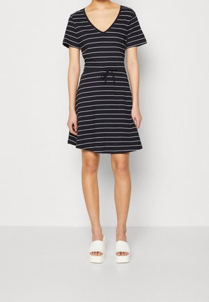Woman wearing a black and white horizontal striped short-sleeve dress with a drawstring waist and white platform slide sandals.
