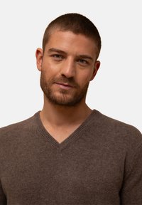 Brauner V-Ausschnitt-Pullover aus Wolle mit einer weichen Textur. Figurbetonter Schnitt mit einem gerippten Ausschnitt. Minimalistischer Stil ohne zusätzliche Muster oder Akzente.