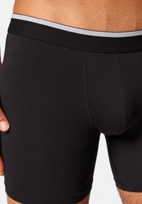 Schwarze Baumwoll-Boxershorts mit glatter Textur, ausgestattet mit einem grauen elastischen Bund und ohne sichtbare Muster oder Akzente.