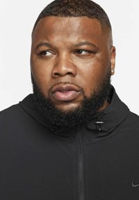 Zwarte jas met ritssluiting en capuchon, met een gladde textuur en verstelbare trekkoorden, afgewerkt met een klein logo bij de kraag.