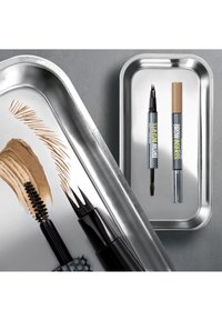 Deux crayons à sourcils avec brosse spoolie et embouts applicateurs à quatre pointes sur des plateaux métalliques, avec des échantillons de couleur marron et des traits fins.