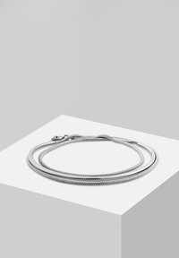 Collier en métal argenté à chaîne serpent flexible composé de trois brins et avec un fermoir à mousqueton. Texture lisse sur toute la surface.