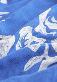 Katoenen stof met een blauwe basis en witte abstracte golfpatronen, met een gestructureerd oppervlak en een zachte draping.