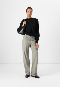 Black, cropped long-sleeve top paired with gray, wide-leg trousers and black loafers. Holding a small black handbag. Minimalist design.