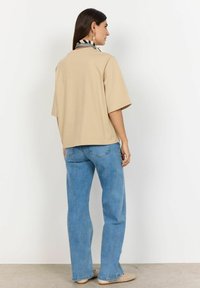 Beige oversized t-shirt med korte ærmer, parret med lyseblå jeans med lige ben. Et sort og hvidt stribet tørklæde er bundet om halsen.