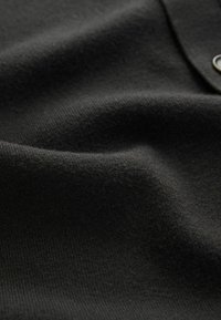 Tejido negro con una superficie suave y ligeramente texturizada. Presenta un sutil acanalado y una caída suave, que enfatizan su flexibilidad.