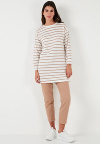 Biely dlhý rukáv s béžovými horizontálnymi pruhmi, v kombinácii s pieskovými nohavicami po členky a bielymi teniskami. Jednoduchý, ležérny dizajn outfitu.