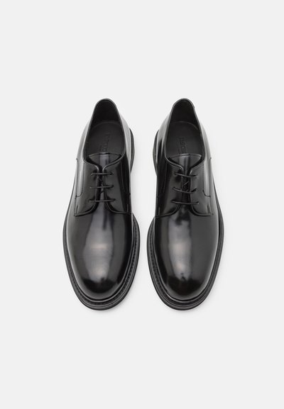 Scarpe in pelle nera con finitura lucida, punta tonda, cinque occhielli per i lacci e suola texture. Design minimalista senza motivi.