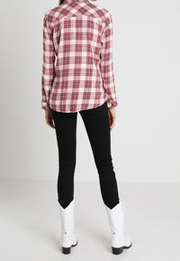 Camicia a quadri rossa e bianca con maniche lunghe, abbinata a jeans skinny neri e stivali western bianchi con punta affusolata.