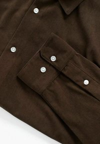 Brun kordfløyelskjorte med krage, lange ermer og sølvknapper. Stoffet har en ribbet tekstur med synlige sømdetaljer.