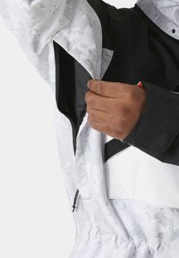 Chaqueta resistente al clima con bloques de color blanco y negro, patrón texturizado, bolsillos con cremallera y puños ajustables.