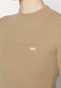 Pull beige côtelé avec un col montant et un petit logo Levi's rose sur le côté gauche de la poitrine. Conçu pour une silhouette ajustée.