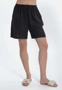 Pantaloni corti neri in lino con vita elastica, caratterizzati da una vestibilità comoda e tasche laterali. Indossati con sandali leggeri senza chiusura.