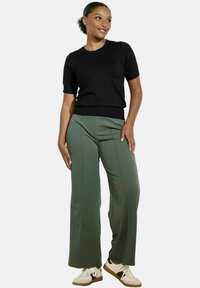 Black short-sleeve sweater paired with high-waisted green trousers featuring a straight-leg design. White sneakers with accents complete the outfit.