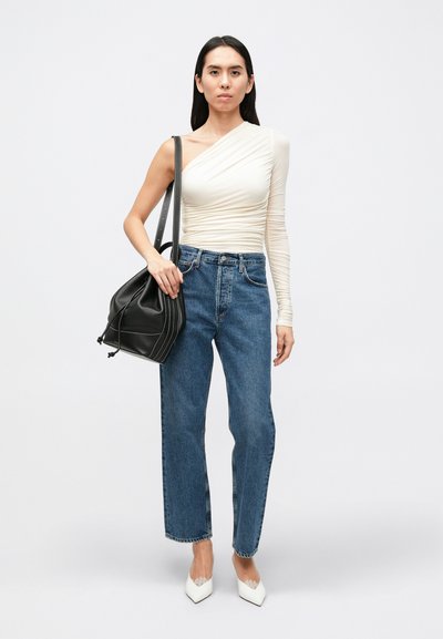 Asymmetrisk off-white top med rynket tekstur, højttaljede blå jeans, sort snørrepose og hvide spidse hæle.
