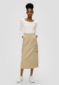 Beige cargorok met een elastische tailleband, zijzakken en een trekkoord. Wit shirt met lange mouwen en geribbelde textuur. Witte sneakers.