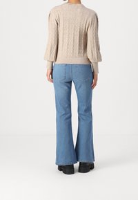 Pull en maille beige avec motif torsadé, manches ballon, associé à un jean évasé bleu clair et des bottes à plateforme noires.