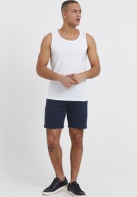 Weißes Baumwolltanktop kombiniert mit marineblauen Shorts und schwarzen sportlichen Sneakers. Die Shorts haben einen einfachen, elastischen Bund.