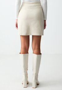 Korte witte bodycon rok gemaakt van een gladde stof, gecombineerd met kniehoge, aansluitende witte leren laarzen met een vierkante hak.