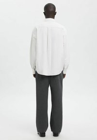 Hvit stripete skjorte med litt buet nederkant og knappelukking, kombinert med mørkegrå vide bukser. Jevn stofftekstur.