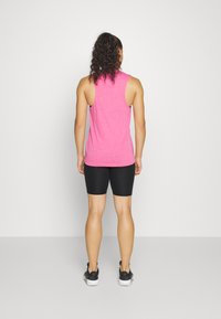 Top aderente rosa con scollatura rotonda e design senza maniche, abbinato a pantaloni ciclistici neri e scarpe sportive nere.