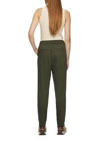 Groene, stoffen joggers met een elastische tailleband en twee achterzakken, met een taps toelopend ontwerp aan de benen, gecombineerd met lichtbruine sneakers.