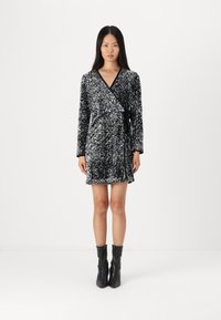 Μαυρένιο παλτό φόρεμα με παγιέτες, μακριά μανίκια και ζώνη στη μέση. Έχει υφή και κοντή γραμμή. Φορεμένο με μαύρες μποτάκια μέχρι τον αστράγαλο.