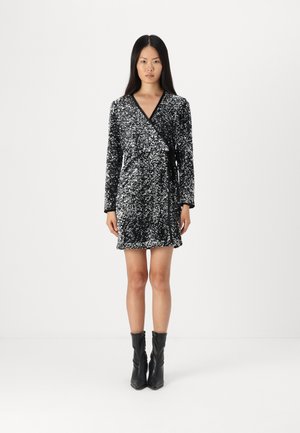 Black sequined wrap dress with long sleeves and a tie waist. Features a textured finish and a short hemline. Worn with black ankle boots.