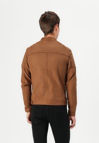 Giacca in suede marrone con colletto, spalle strutturate e cuciture; vestibilità slim, dotata di chiusure a scatto in vita e ai polsini.