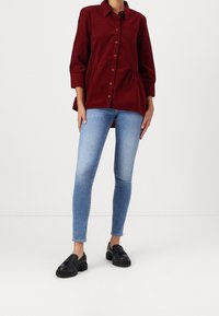 Bordeaux corduroy button-up shirt met een peplumdesign, gecombineerd met lichtblauwe skinny jeans en zwarte loafers.