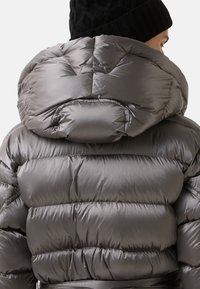 Polstret pufferjakke i metalgrå med høj krave og indsnøret talje. Glat, skinnende tekstur med quiltede sektioner til isolering.