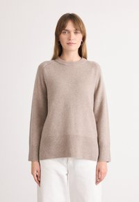 Beige pletený svetr s kulatým výstřihem, dlouhými rukávy, žebrovaným lemem a dekorativními švy na ramenou. Hladká textura.