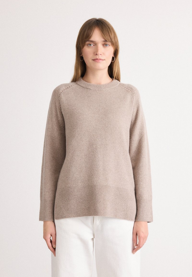 Maglione beige lavorato a maglia con scollo rotondo, maniche lunghe, orlo a costine e dettagli decorativi a punto sulle spalle. Texture liscia.