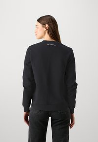 Felpa nera con maniche lunghe, polsini e orlo a coste, con il logo "KARL LAGERFELD" sopra il colletto, texture liscia, vestibilità casual.